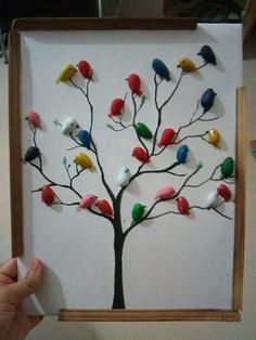 a person holding up a paper tree with colorful birds on it