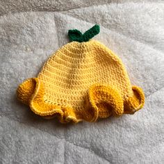 a crocheted yellow hat with a green bow on the top sitting on a white blanket