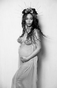 a pregnant woman in a dress posing for a black and white photo with flowers on her head