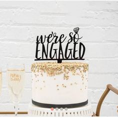 there is a cake with the words we're engaged on it and two glasses next to it