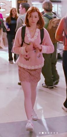 a woman is walking through an airport with her hand on her hip while wearing a pink sweater and fringe skirt