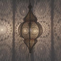 an intricately designed lantern hanging from the ceiling in front of a curtained wall