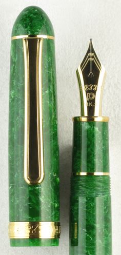 a green and gold fountain pen sitting on top of a white table next to a bottle