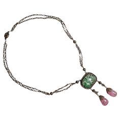 Created just after the turn of the century (circa 1917), this gilt silver jadeite and tourmaline drop necklace was created in China for the export market. Intricately detailed wirework that today would be nearly impossible to create by hand was executed with consummate skill by the early twentieth-century jeweler who created this piece. Even the back is strikingly beautiful. Elaborate wirework balls are stationed along the chain together with white glass beads. The necklace measures 18.5 inches in length. The jade and tourmaline drop hangs an additional 2 ¾ inches. The carved and pierced jadeite jade plaque is a mottled green and the two pink tourmaline drops that are suspended from the jade are without chips are cracks. Minor losses to the wirework topping each tourmaline gem do not mitig Antique Jade Pendant Necklace, Vintage Jade Necklace With Natural Stones, Elegant Jade Cabochon Necklace, Vintage Briolette Necklace For Formal Occasions, Vintage Jade Pendant Jewelry, Vintage Oval Jade Necklace, Vintage Natural Stone Necklace For Formal Occasions, Art Nouveau Gemstone Necklace For Formal Occasions, Vintage Natural Stones Necklace For Formal Occasions