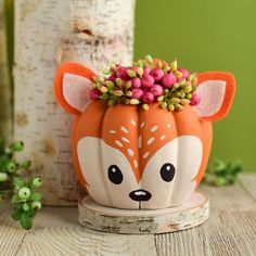 an orange and white pumpkin decorated like a fox with flowers on its head sitting next to a tree