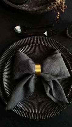 a black plate topped with a bow tie next to utensils and silverware