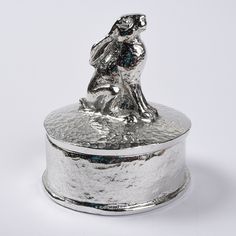 a silver box with a metal figure on it's lid, sitting on a white surface