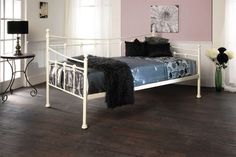 a white metal bed frame in a bedroom with hardwood floors and pink walls, along with black pillows