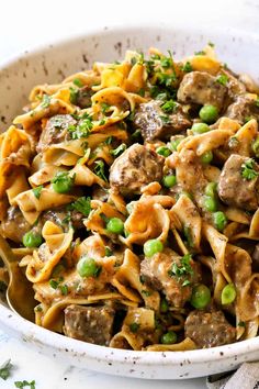 a white bowl filled with pasta, peas and meatballs on top of a table