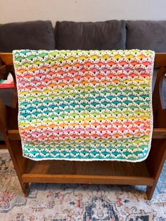 a multicolored crocheted afghan on a wooden stand in front of a couch