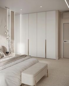 a large white bed sitting in a bedroom next to a wall mounted cabinet and footstool