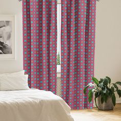 a bed sitting next to a window covered in pink and blue curtains with flowers on them