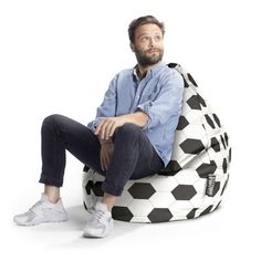 a man sitting on a soccer ball shaped bean bag chair with his legs crossed and feet crossed