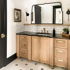 a black and white tiled bathroom with wooden cabinetry, sink and mirror on the wall