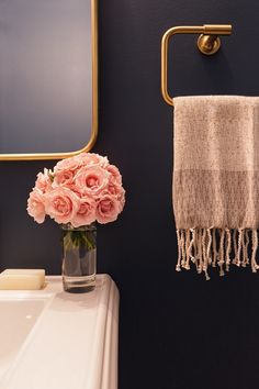 a pink flower in a glass vase next to a towel rack and mirror on the wall