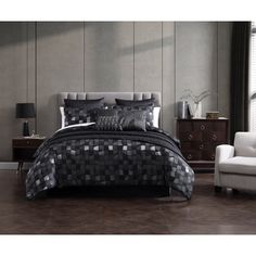 a bed with black and silver comforters in a room next to a white chair