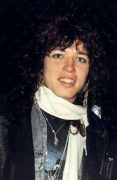 a woman with curly hair wearing a black leather jacket and white scarf posing for the camera