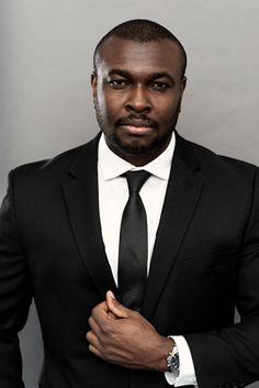 a man in a black suit and tie posing for a photo with his hands on his chest