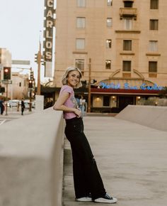 a woman standing on the side of a building next to a street with buildings in the background