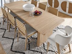 a dining room table with chairs and fruit on the plate next to it, in front of a large window