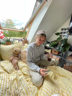 a woman sitting on top of a bed next to a teddy bear and holding a cell phone