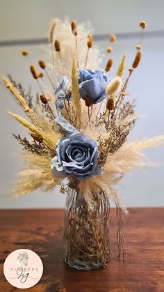 Enhance your home decor with our stunning Cornflower Blue Rose Bloom Table Vase. This exquisite arrangement features high-quality mesh fabric, vibrant caspia, meadow blooms, and yellow bunny tails, all elegantly displayed in a thick, high-quality glass vase. The rustic Boho style adds a charming touch, making it a versatile piece that complements any room. This beautiful vase is ideal for a classic table setting as a centerpiece for weddings, events, or any special occasion. It's a wonderful add Gold And Blue Wedding Centerpieces, Western Style Wedding Centerpieces, Blue Rose Centerpiece, Blue Centrepiece Ideas, Rustic Elegant Centerpieces, Vintage Glass Centerpieces, Gold And Blue Centerpieces, Blue Pampas Centerpiece, Slate Blue Wedding Decor