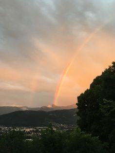 a rainbow in the sky over some trees and buildings with mountains in the back ground