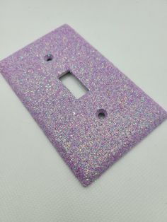 a light switch cover with purple and silver glitter on the bottom, sitting on a white surface