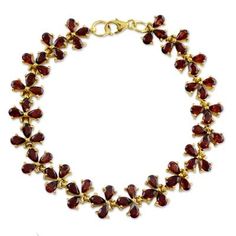 a gold bracelet with red glass beads and leaves on the clasp, set against a white background