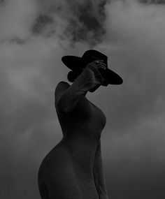 a black and white photo of a woman with a hat on her head looking up into the sky