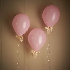 three pink balloons with gold bows hanging from the ceiling in front of a beige wall