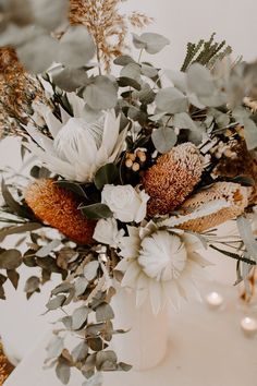 a vase filled with flowers and greenery on top of a white table cloth covered table