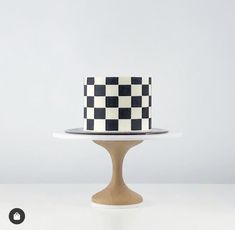 a black and white checkered cake sitting on top of a wooden stand next to a wall