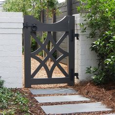 a black gate is open in front of a white brick wall and shrubbery on the other side