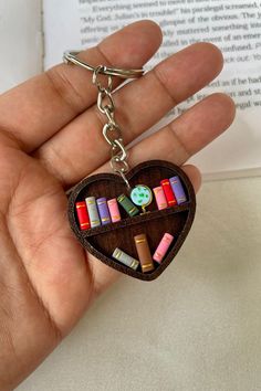 a hand holding a wooden heart shaped keychain filled with books