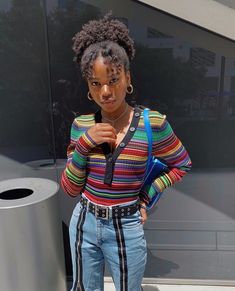 a woman standing next to a trash can wearing jeans and a striped shirt with suspenders