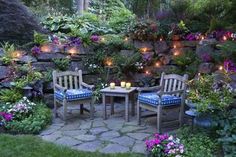 two wooden chairs sitting on top of a stone patio surrounded by flowers and greenery