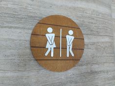 a wooden sign on the side of a building showing two men in toilet stalls, one standing up