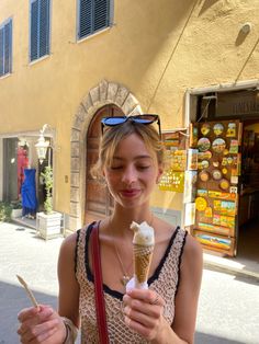 a woman holding an ice cream cone in her hand and looking down at the ground