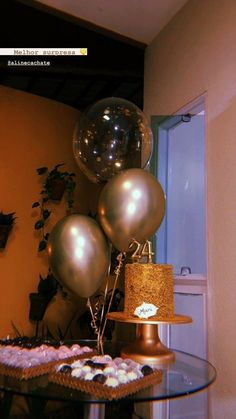 a table topped with lots of balloons next to a cake on top of a glass table