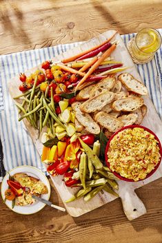 a wooden table topped with plates of food next to bread and veggie platters