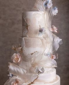 a three tiered cake with white frosting and flowers on the top, surrounded by feathers