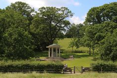 two people sitting on park benches in front of a gazebo and grassy area with trees