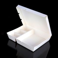 an open white box sitting on top of a black surface with its lid opened and two compartments closed