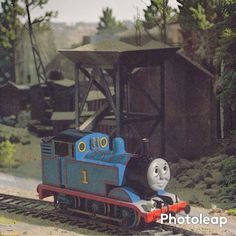 a thomas the tank engine train on tracks in front of a wooden structure and trees