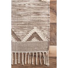 a brown and white rug with tassels on the floor next to a wooden wall