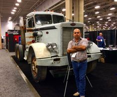 a man standing in front of a large truck on display at an exhibition or show