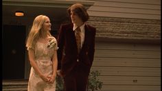 two young people dressed in formal wear standing next to each other on the porch of a house