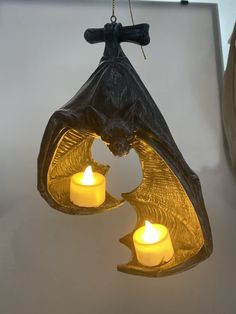 two candles are lit in the shape of a bat hanging from a hook on a wall