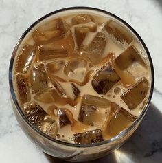 a glass filled with ice and liquid on top of a marble countertop next to a metal spoon